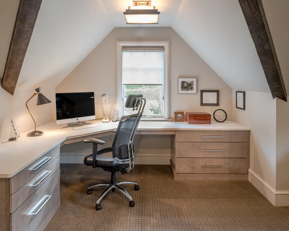 A fitted desk and drawers sit below a sloping roof around a small window