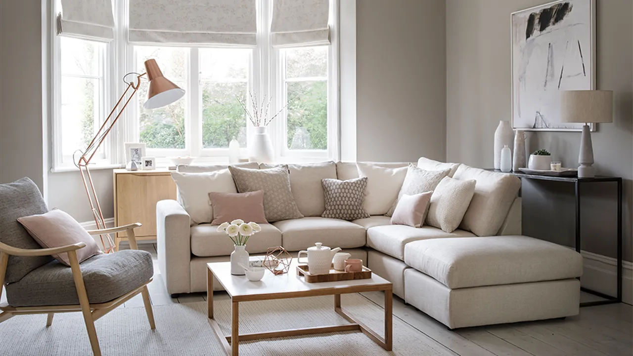A pale beige sectional sits beneath a broad window beside a timber coffee table