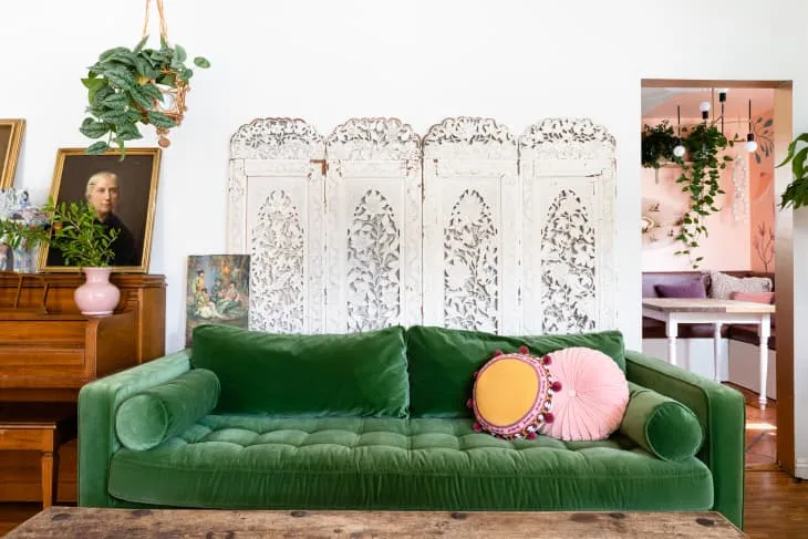 A green sofa sits in front of a pale folding screen with an ornate pattern