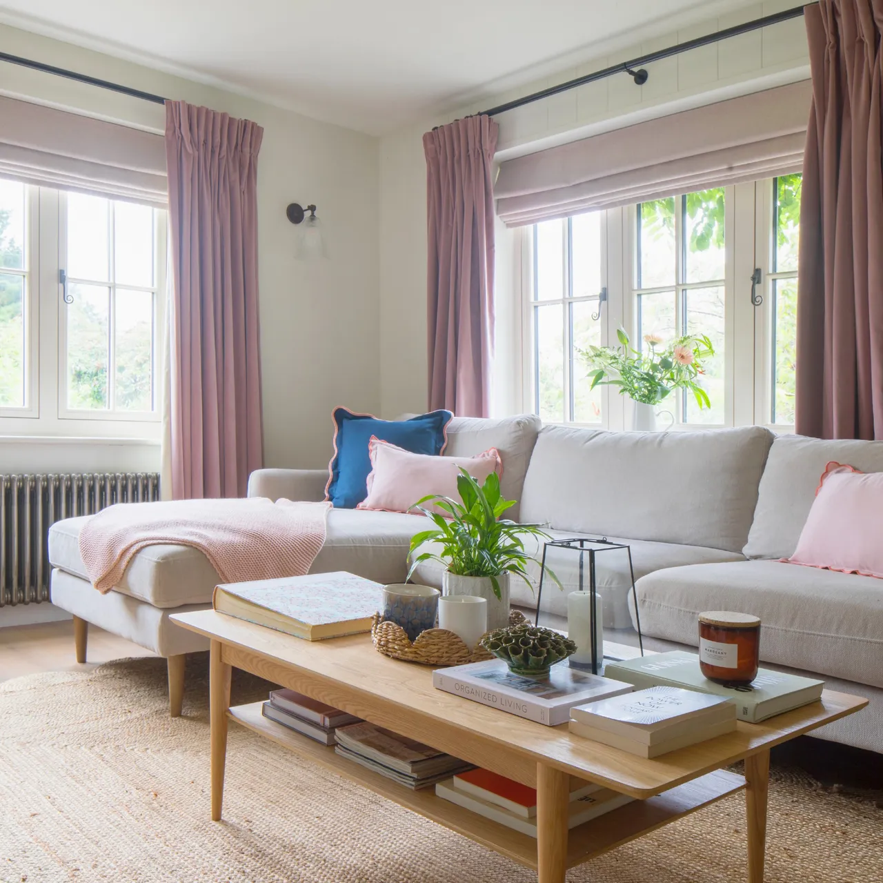 A pale sectional sits beneath broad windows beside a slim wooden coffee table